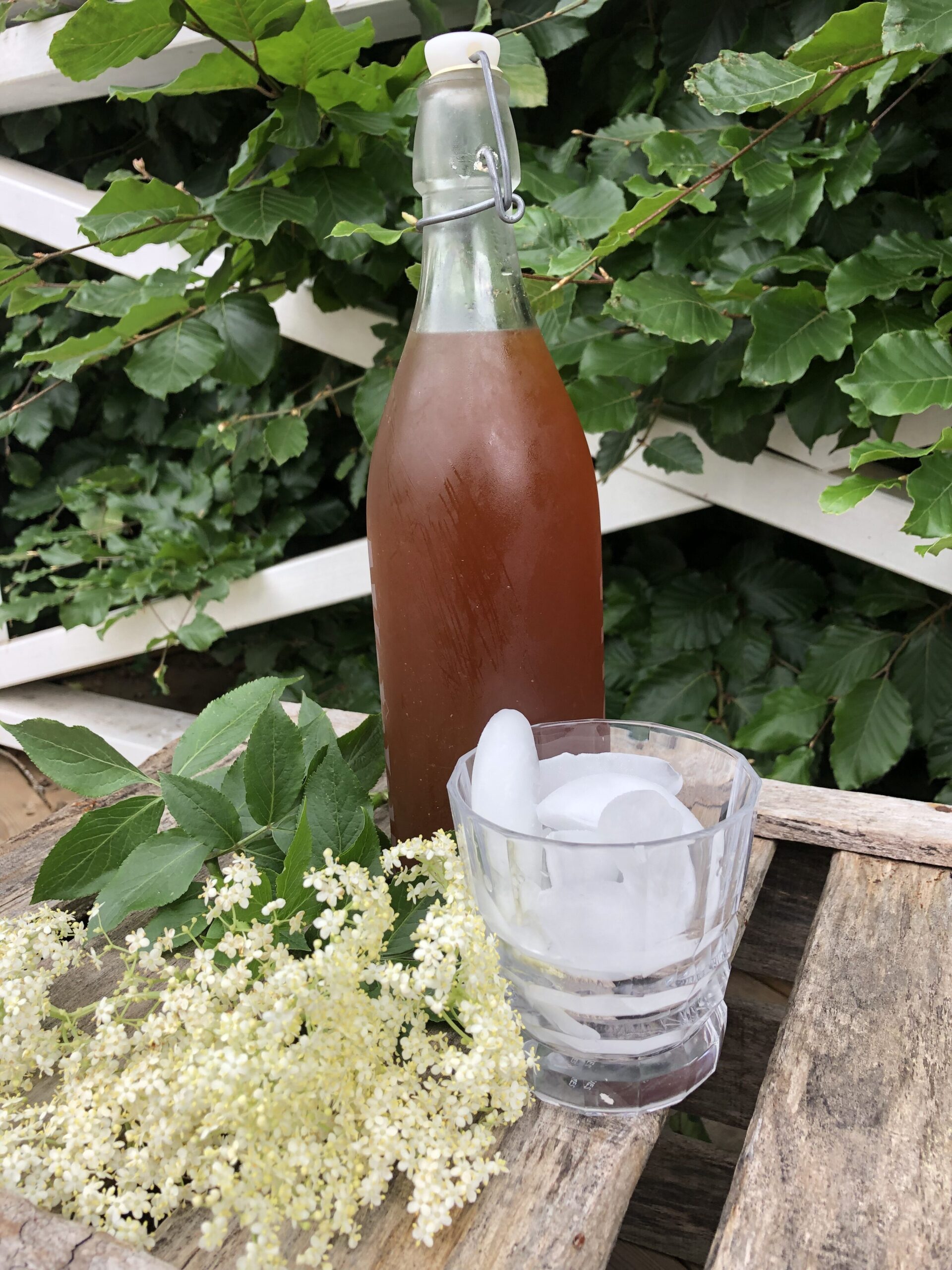 Hjemmelavet hyldeblomstsaft i en flaske med et glas med isterninger foran