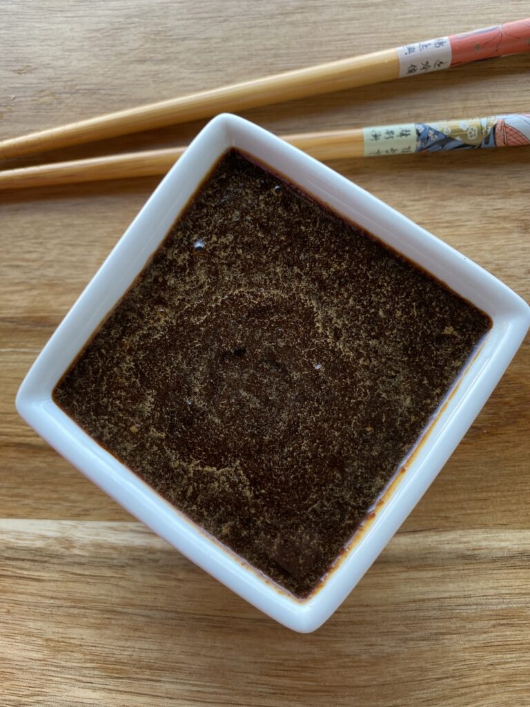 Teriyaki sauce i en firkantet skål med spisepinde ved siden af