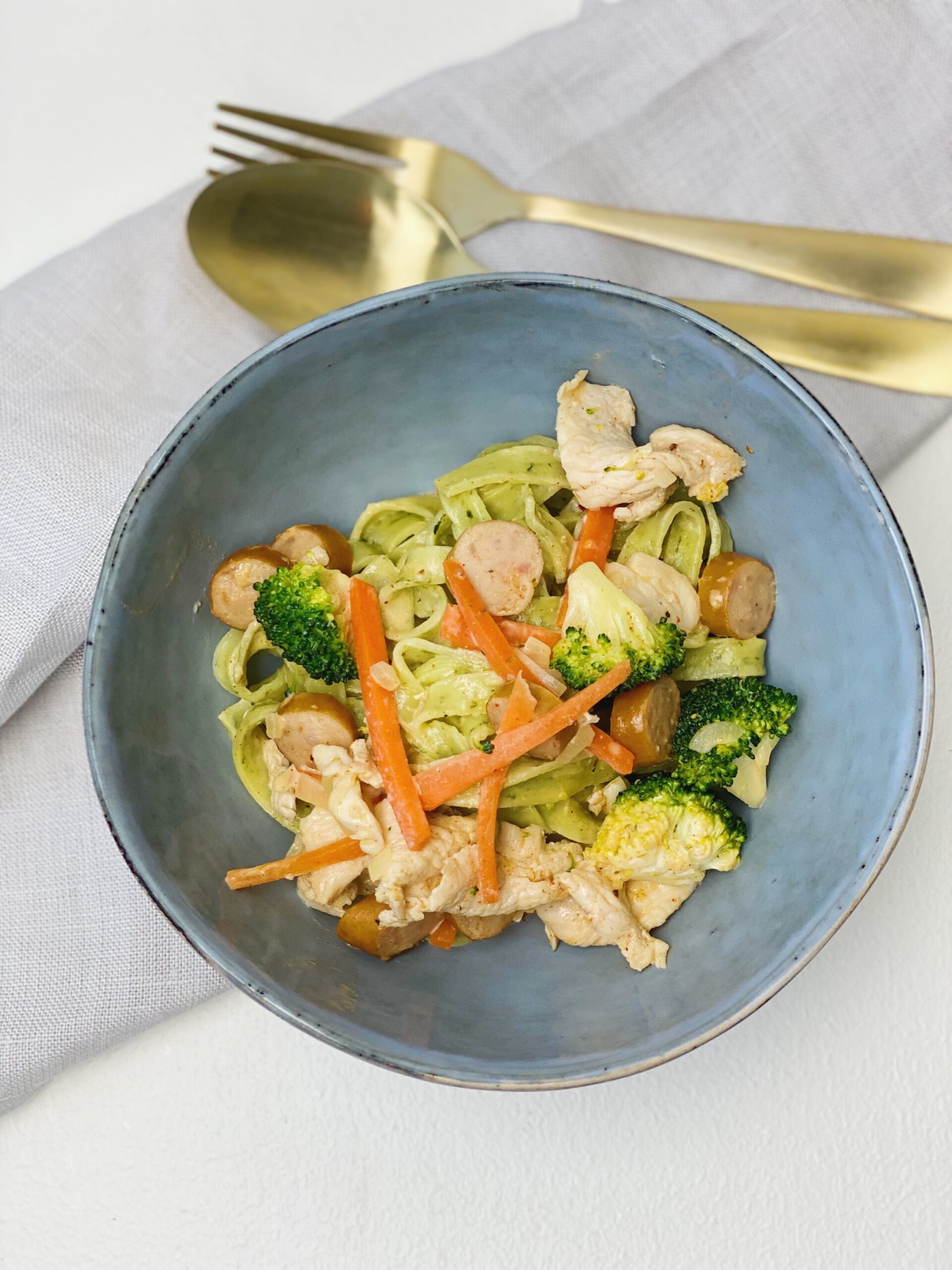 cremet spinatfettuccine med kylling og pølser i en skål
