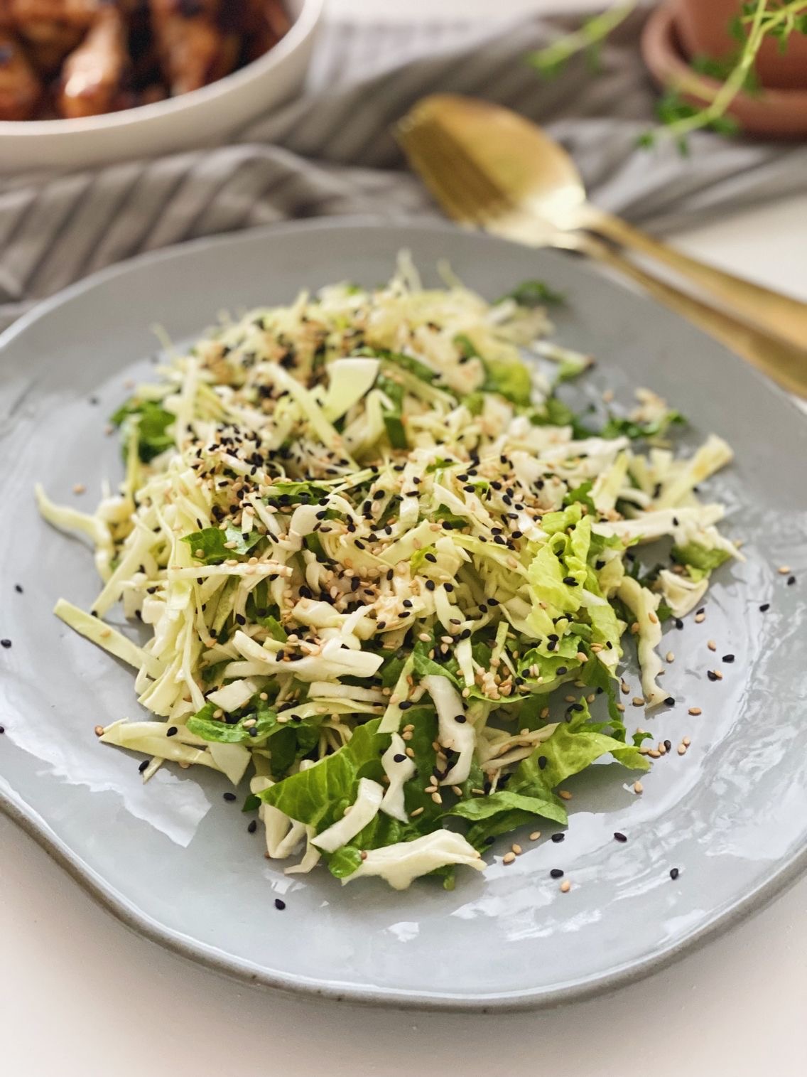 Spidskålsalat med ingefærdressing på et gråt fad set oppefra med kyllingevinger og frisk timian i en lerpotte i baggrunden