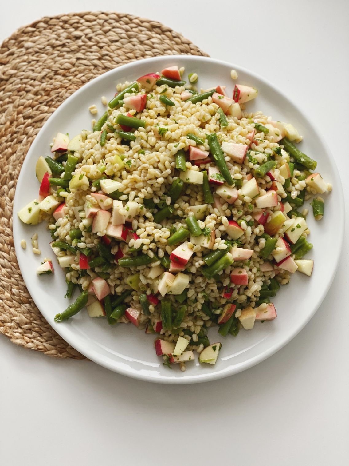 Hvedekernesalat med bønner, æbler og persille vendt i den lækreste vinaigrette set oppe fra. Den er anrettet på et rundt fad