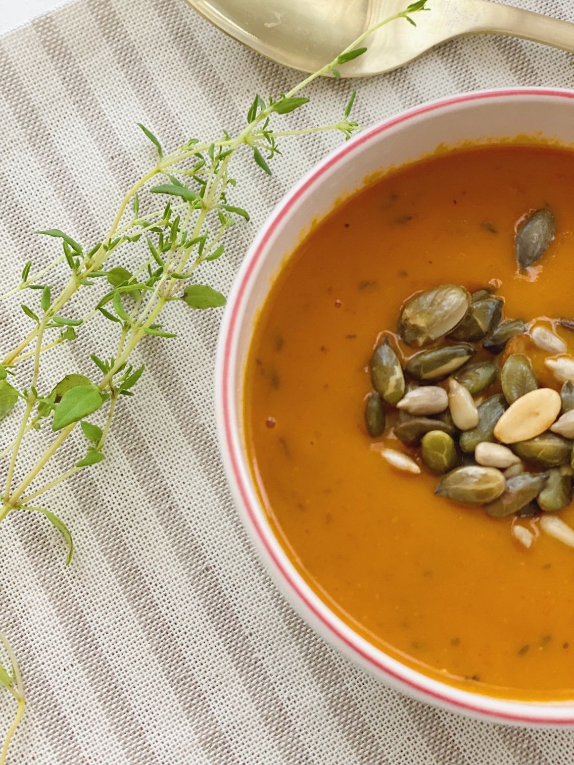 Tomatsuppe set tættere på, så man kun kan se halvdelen af koppen. En klud ved siden af og en dusk timian