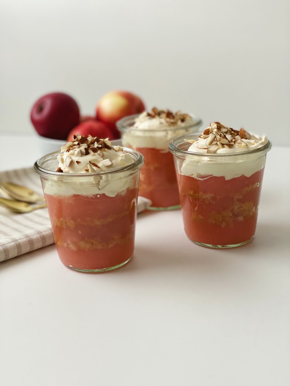 Æblekager i høje portionsglas med en skål med røde æbler i baggrunden