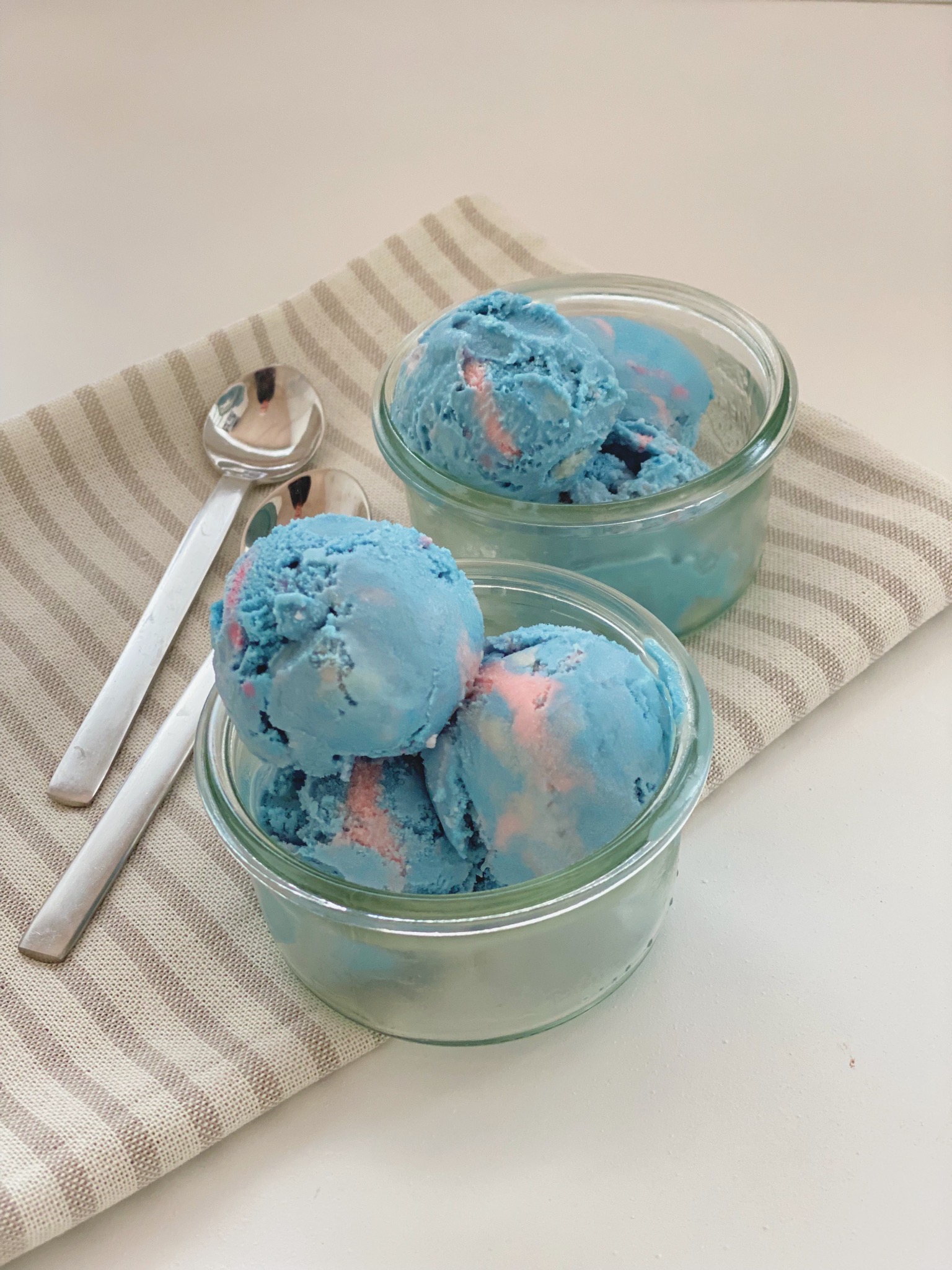 Tyggegummi is i to glasskåle set ind fra siden af og med en stribet serviet og to teskeer ved siden af. Isen er lyseblå og lyserød