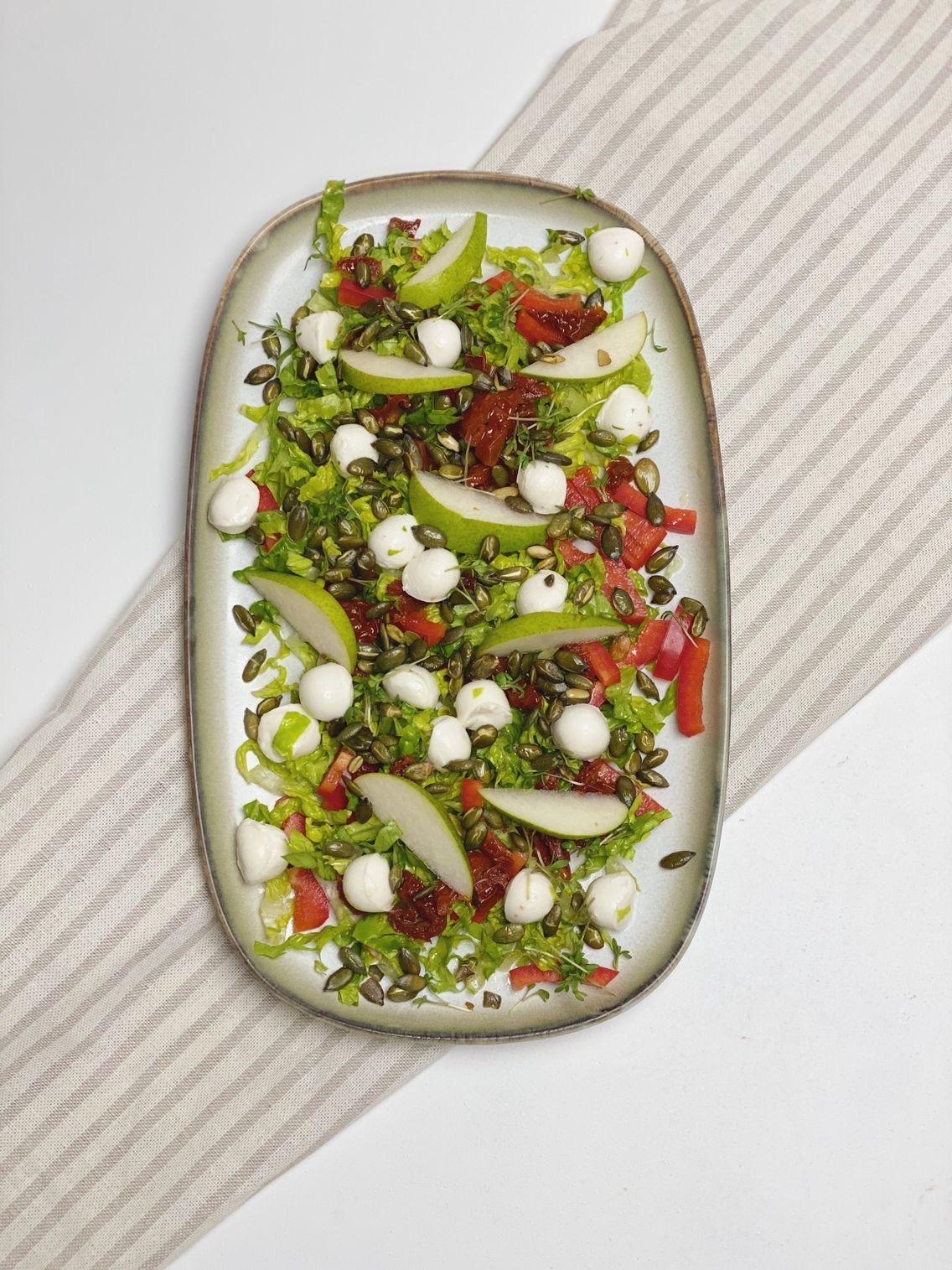 Salat med pære og mozzarella som er anrettet på et aflangt fad som er placeret oven på en stribet serviet. Det hele ses ovenfra.