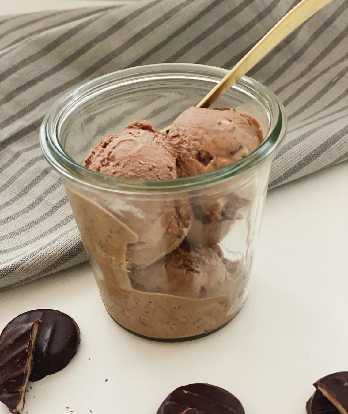 Mint chokoladeis i en høj glasskål med en guldske i. Der ligger mint chokoladeknapper ved siden af glasset med is i. Det er de samme mint chokoladeknapper som der er i isen.
