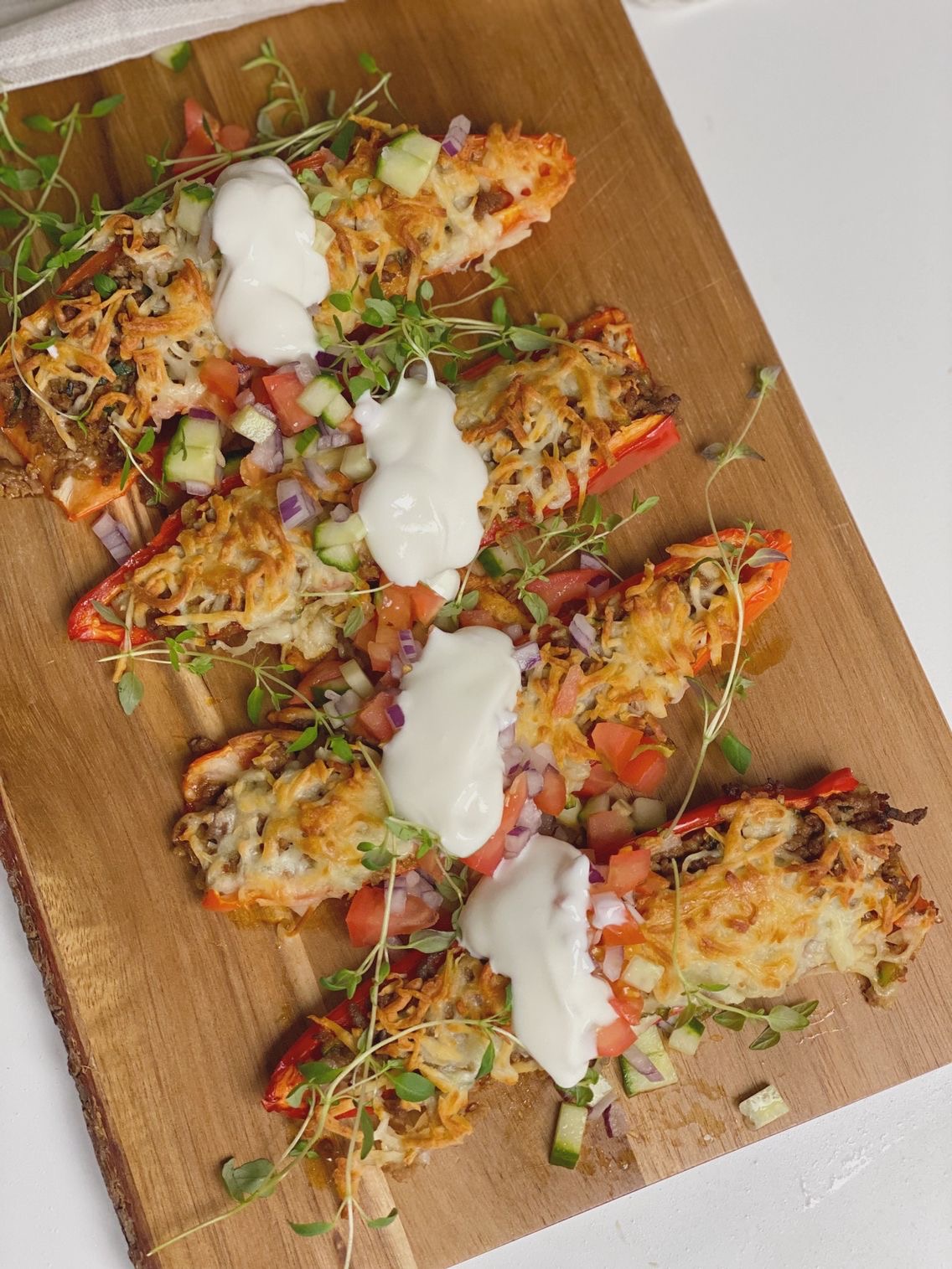 Fyldte snackpeber med tomatsalat og en klat cremefraiche på. Billedet er taget oppefra og du ser kun de fyldte snackpebre på skærebrættet.