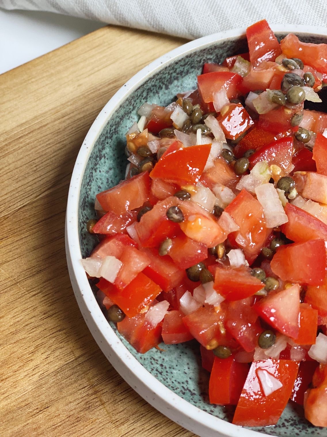 En tomatsalat med de marinerede grønne linser i sammen med små tern af løg. Salaten er i en grøn skål og det er set tæt på
