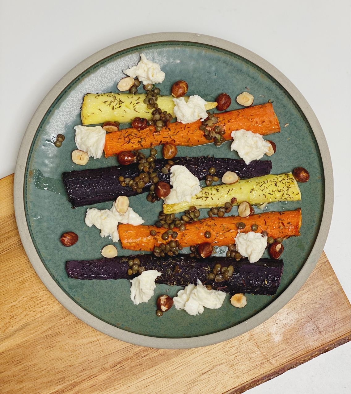 De marinerede grønne linser brugt oven på nogle stegte gulerødder som er i farverne lys gul, orange og lilla. sammen med mozzarella og ristede hasselnødder. Det hele er på en grøn tallerken