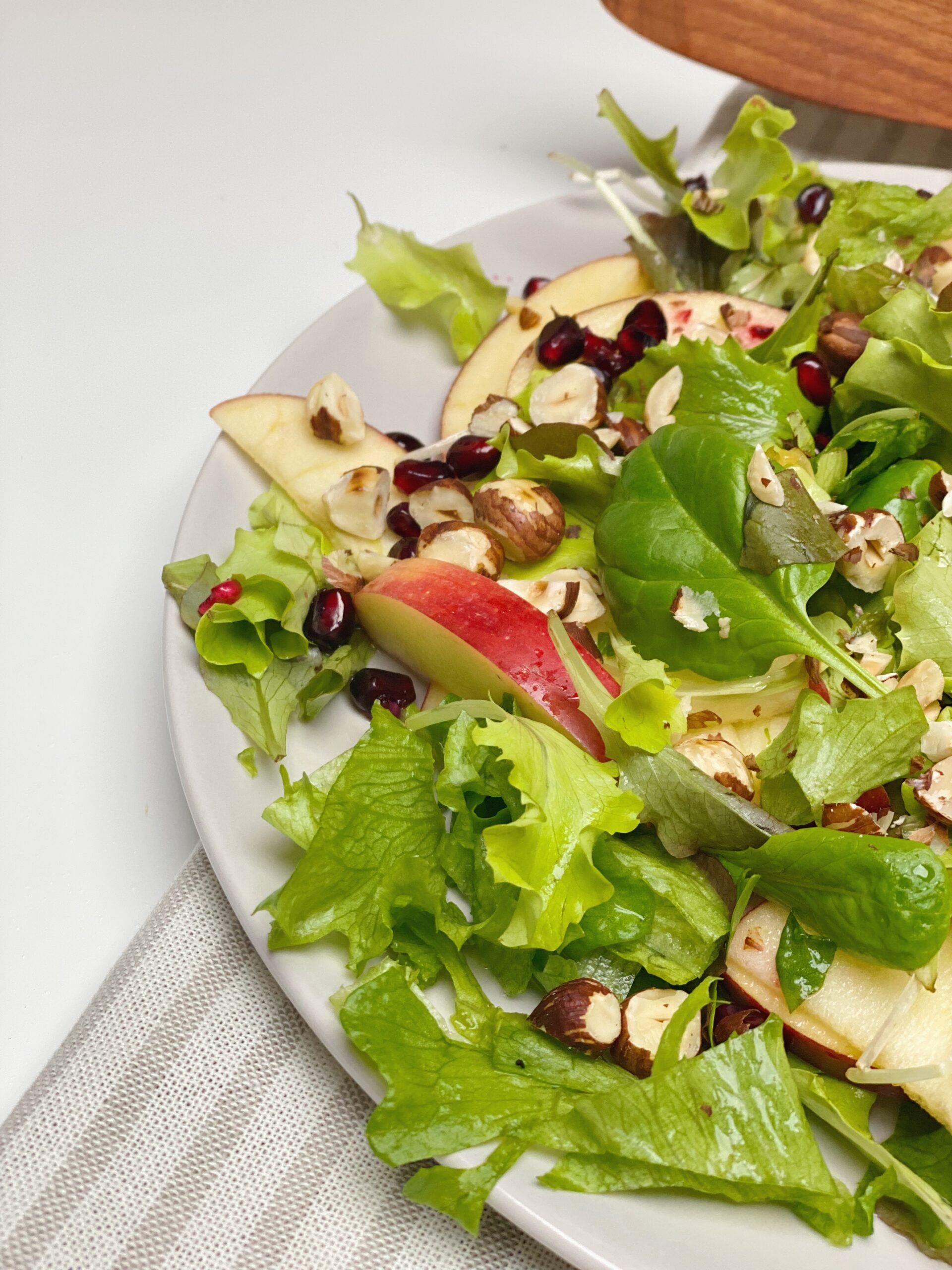 Salat med appelsinvinaigrette set tæt på, hvor man kun kan se halvdelen af tallerkenen. I baggrunden ligger der en salattang og tallerkenen står oven på en stribet serviet.