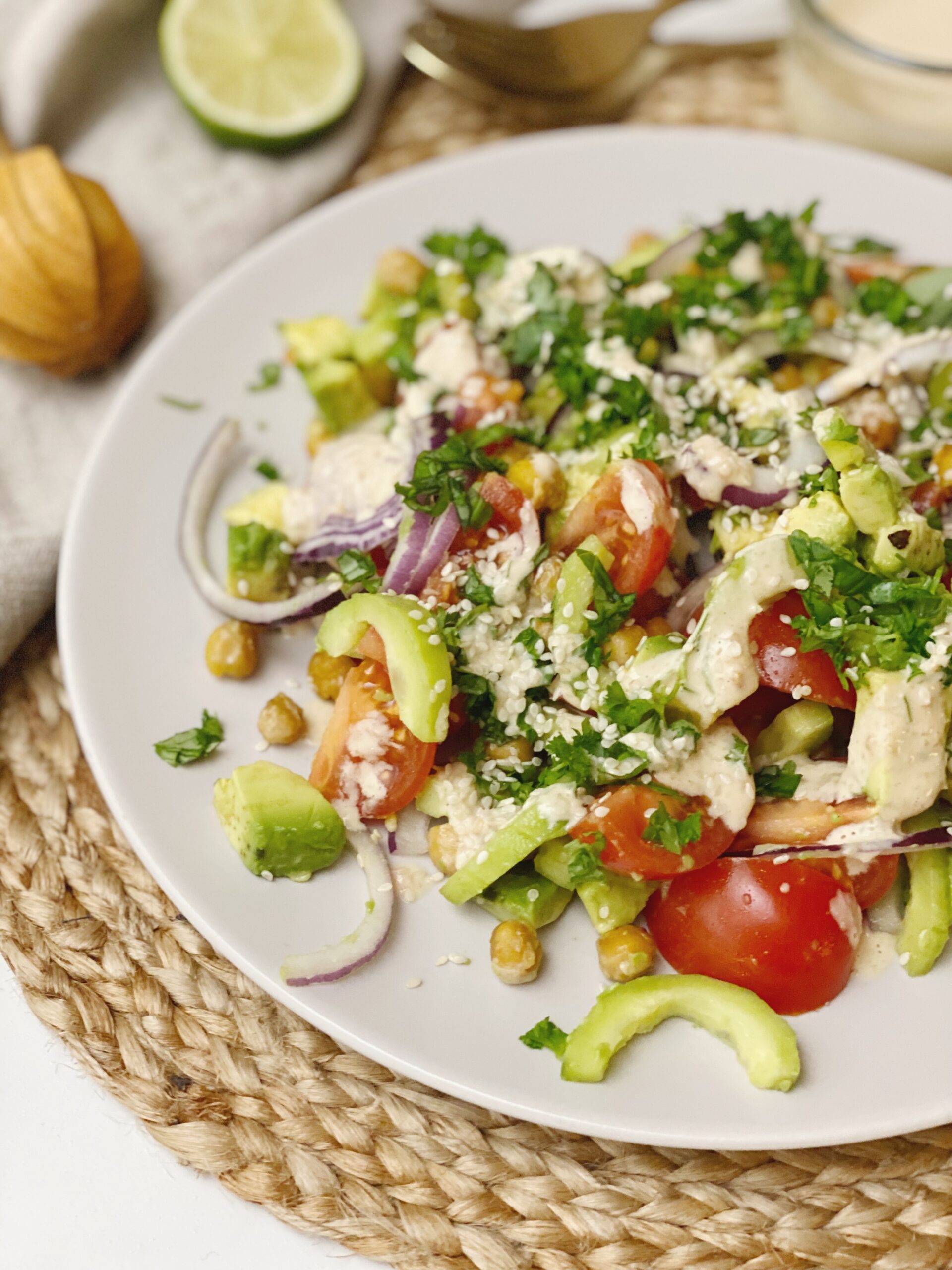 Den mellemøstlig inspireret salat med tahindressing set tæt på på en tallerken. Man kan se en citruspresser i træ og en halv limefrugt i baggrunden.
