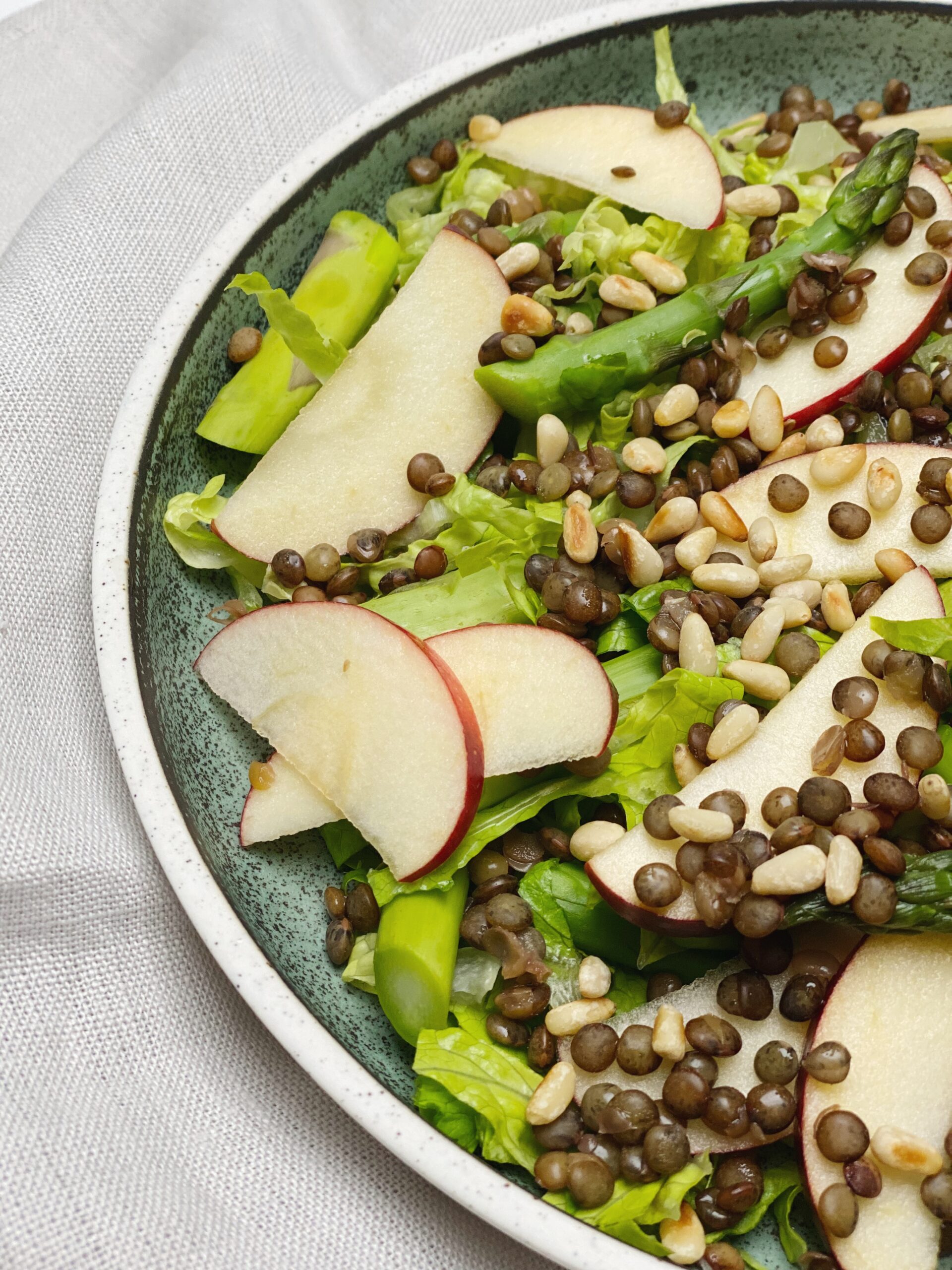 Salat med grønne linser på en grøn tallerken, hvor du kun ser halvdelen af tallerkenen tæt på.