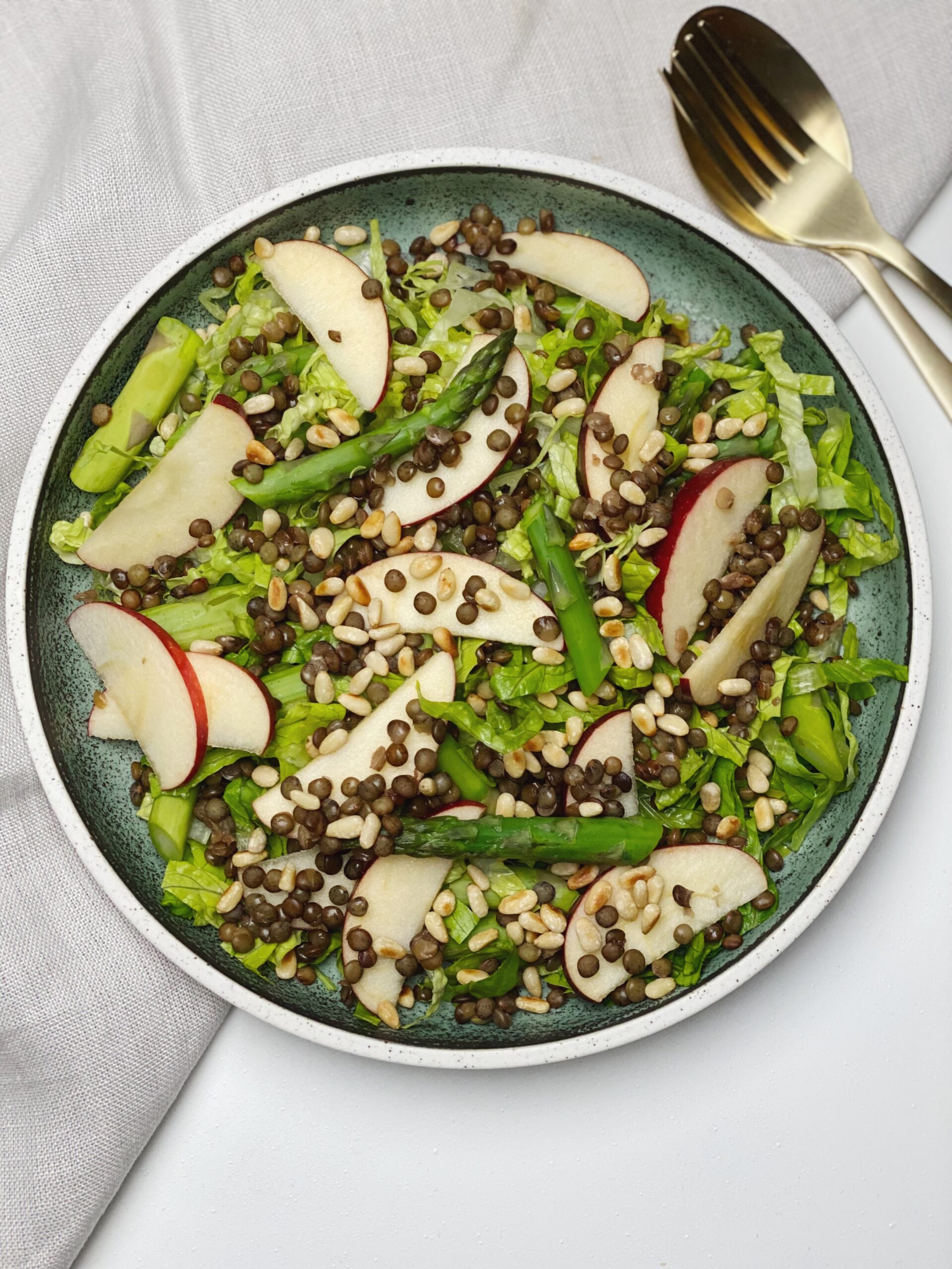 Salat med grønne linser set oppefra så man ser hele tallerkenen og der ligger en guld ske og gaffel ved siden af