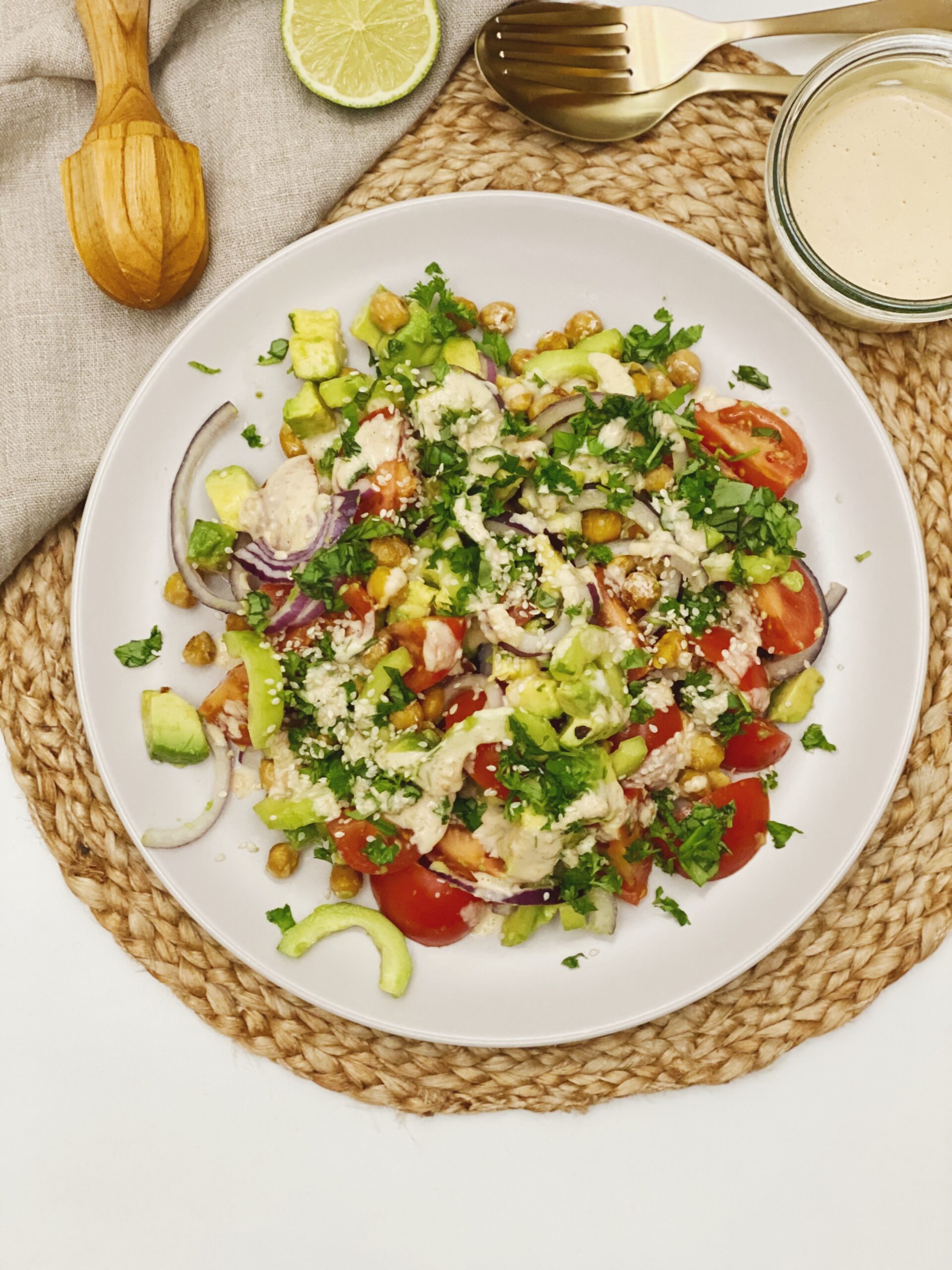 Den mellemøstlig inspireret salat med tahindressing set oppefra på på en tallerken. Man kan se en citruspresser i træ, en lille skål med tahindressing og en halv limefrugt ved siden af.