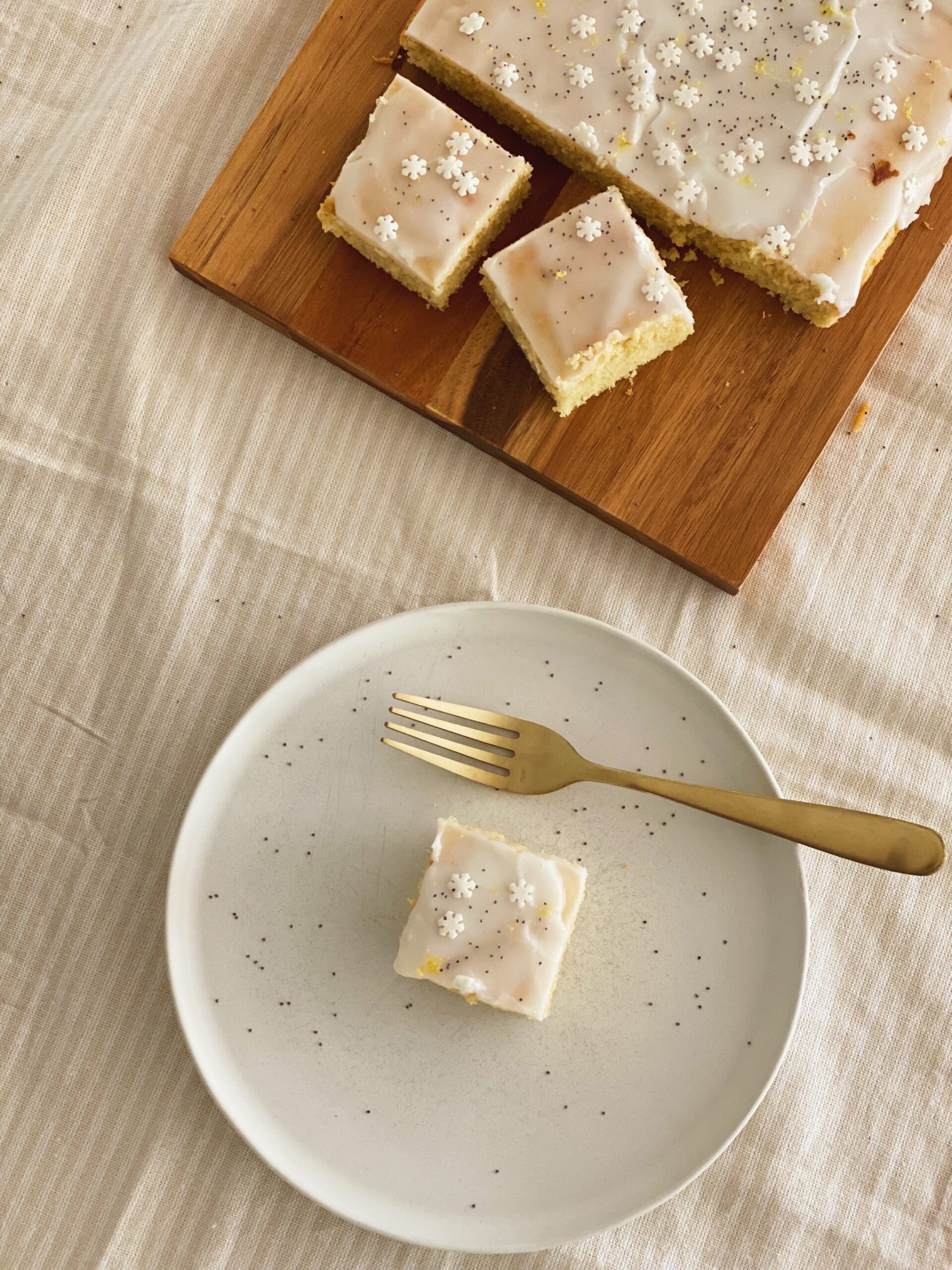 En tallerken med et stykke citronkage på og et spækbræt med resten af citronkagen på. Det hele er set oppefra