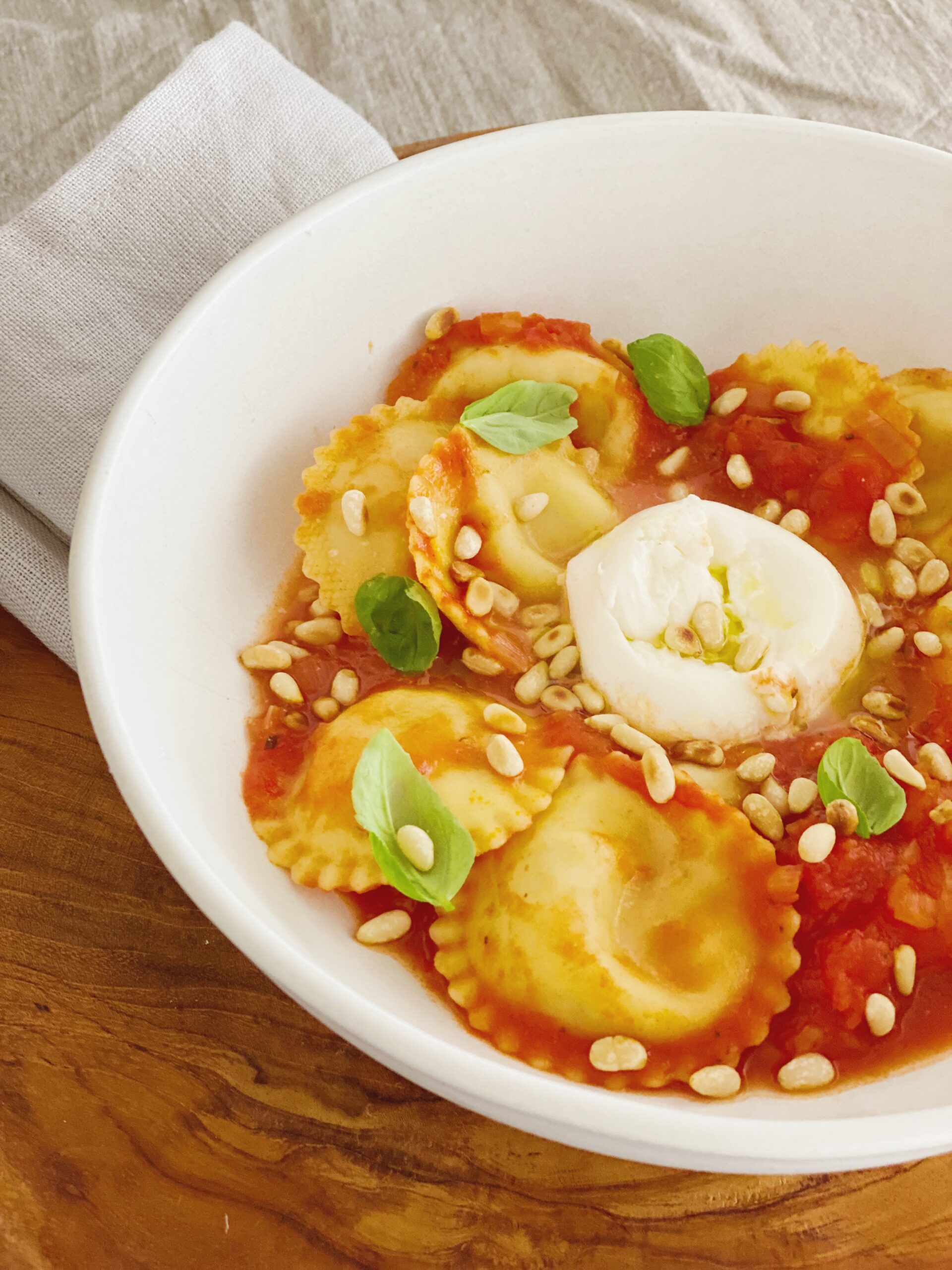 Ravioli med tomat og burrata set tæt på. Retten er anrettet i en hvid skål som står på et rundt træfad