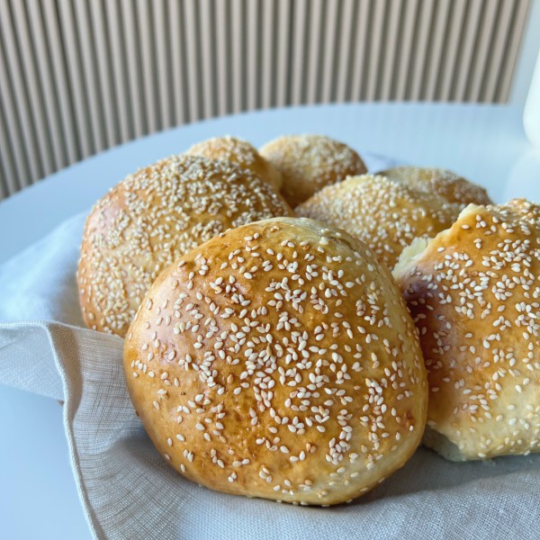 Burgerboller med danskvand set tæt på. De står på et fad med en stofserviet i bunden. De står på et hvidt bord med en akustikvæg i baggrunden.