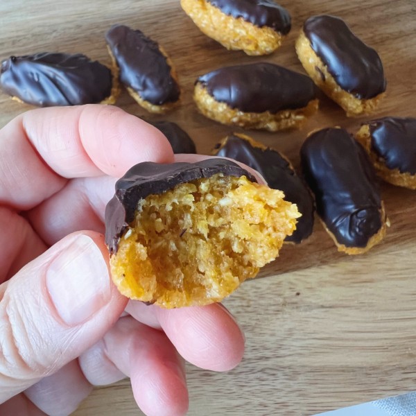 En abrikosbar med chokolade som bliver holdt mellem to fingre og der er taget et bid af den